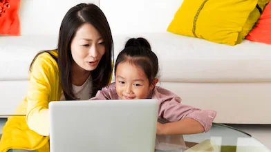 Older woman sitting with child at coffee table, looking at a tablet.